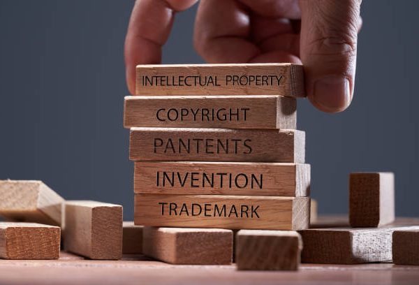 man adding a  block showing the words Intellectual property on top of  other wooden block with text copyright, patents,  invention,and trademark